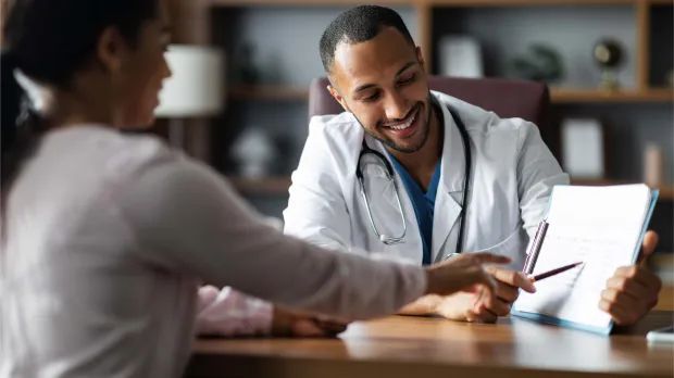 Doctor consulting with patient in UAE healthcare setting Smiling doctor meeting with a patient, reviewing medical information together — representing access to quality private healthcare through group medical insurance in the UAE.